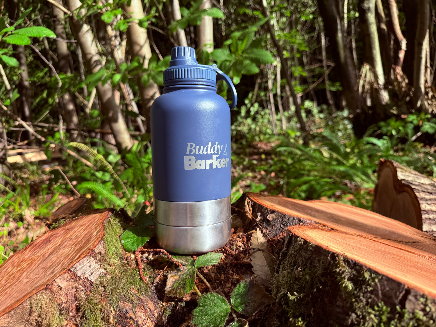 Blue Trail dog travel bottle with 'Buddy Barker' branding on a log in a forest setting