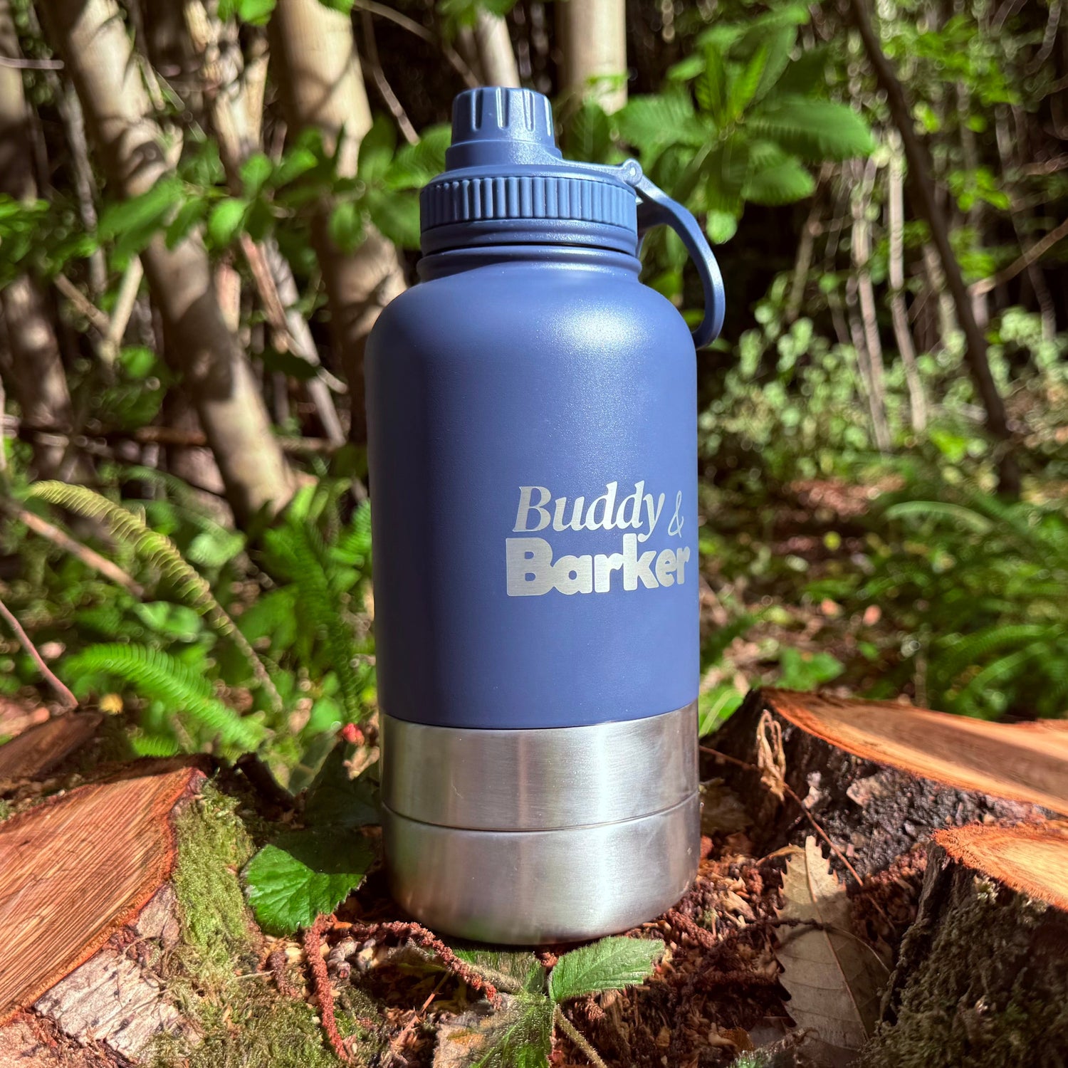 Blue Trail dog travel bottle with 'Buddy Barker' branding on a log in a forest setting