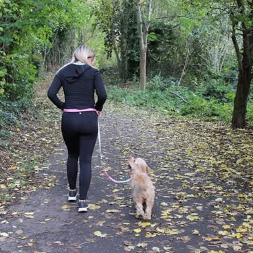 Woman walking a dog on a path in a forest with the Hands Free lead around her waist.