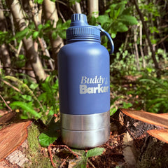 Blue Trail dog travel bottle with 'Buddy Barker' branding on a log in a forest setting